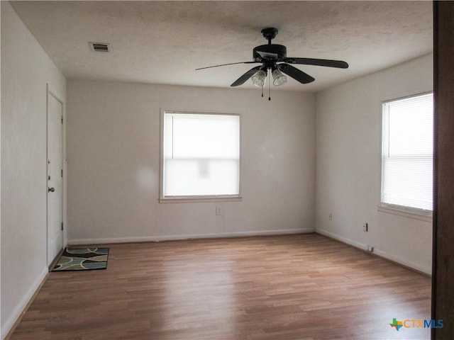 unfurnished room featuring a ceiling fan, baseboards, visible vents, and wood finished floors