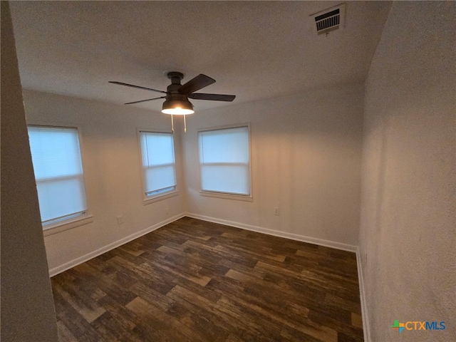 empty room featuring visible vents, a ceiling fan, dark wood-style flooring, and baseboards