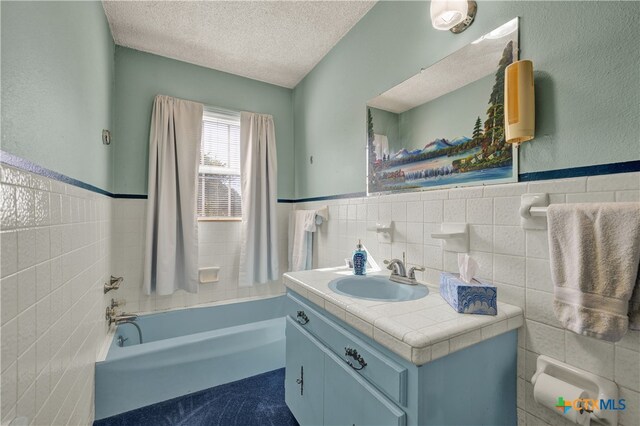 bathroom featuring vanity, a washtub, tile walls, and a textured ceiling