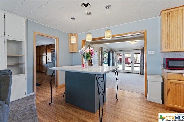 kitchen featuring a kitchen bar, decorative light fixtures, french doors, and light hardwood / wood-style flooring