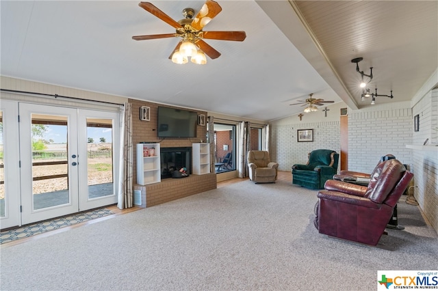 living room with french doors, lofted ceiling with beams, ceiling fan, a fireplace, and brick wall