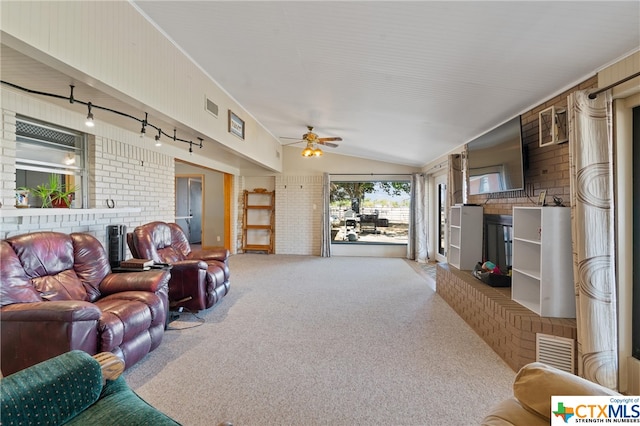 carpeted living room with track lighting, wooden walls, lofted ceiling, ceiling fan, and brick wall