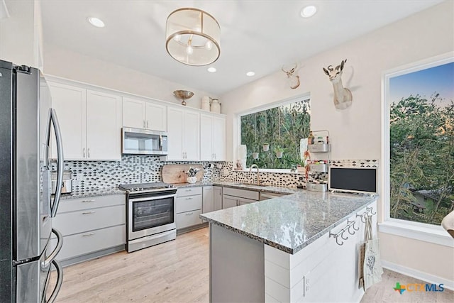 kitchen with a peninsula, appliances with stainless steel finishes, light stone counters, and decorative backsplash