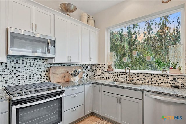 kitchen with stainless steel appliances, light stone counters, backsplash, and a sink