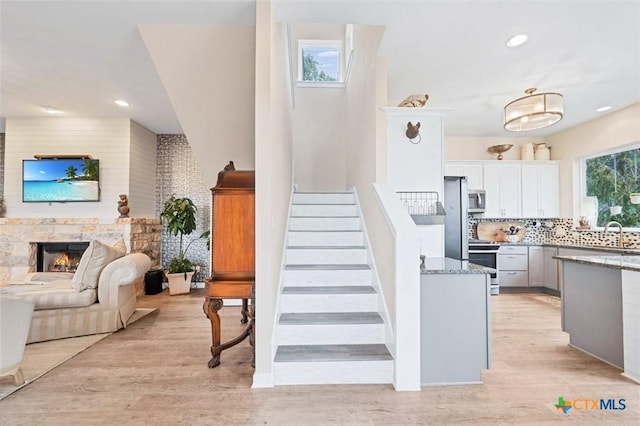 kitchen featuring a warm lit fireplace, light wood-style flooring, appliances with stainless steel finishes, light stone countertops, and backsplash