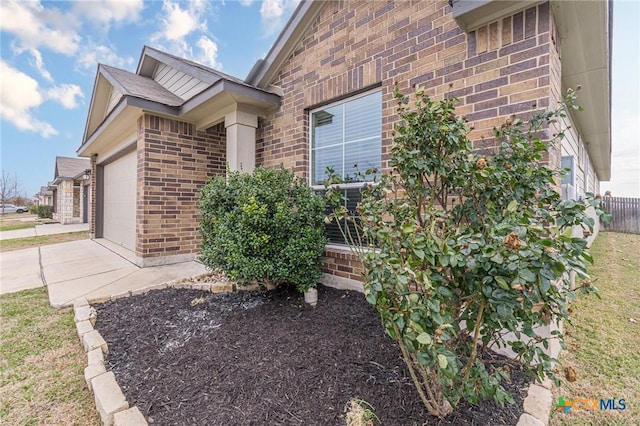 exterior space with brick siding, concrete driveway, a garage, and fence