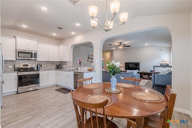 dining space with arched walkways, visible vents, ceiling fan, and vaulted ceiling