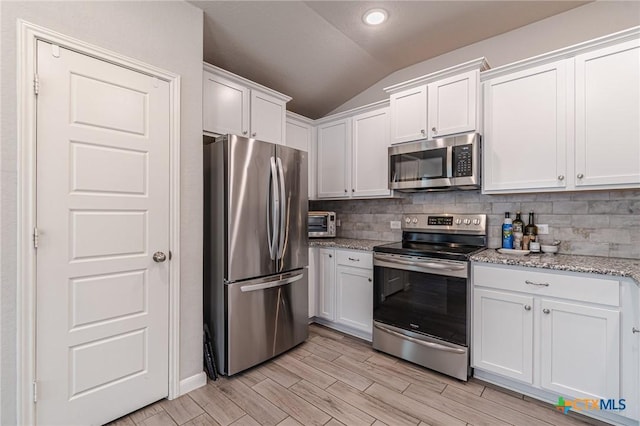 kitchen with stainless steel appliances, lofted ceiling, backsplash, and white cabinets