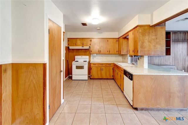 kitchen featuring light tile patterned floors, white appliances, wooden walls, and sink