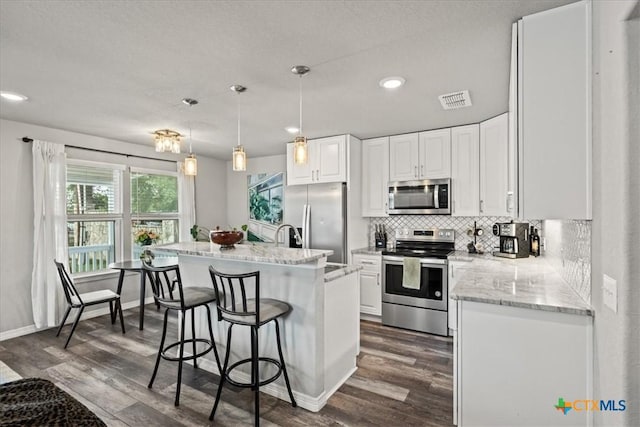 458 Seele St, New Braunfels, TX 78130 - kitchen with stainless steel appliances, dark wood-style floors, white cabinets, tasteful backsplash, and a kitchen bar