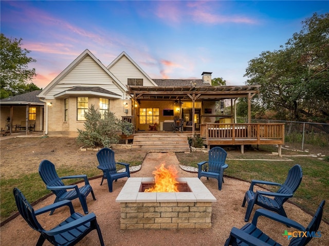 rear view of property with an outdoor fire pit, brick siding, fence, and a deck