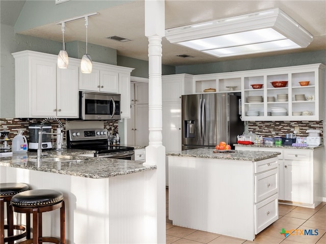 kitchen with light tile patterned floors, stainless steel appliances, decorative backsplash, white cabinets, and a peninsula