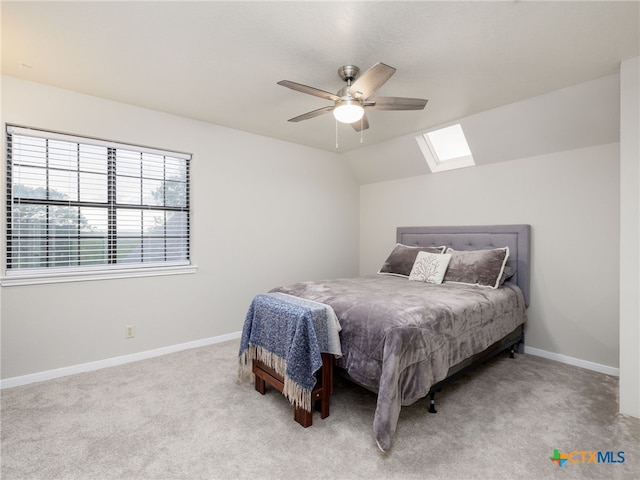 carpeted bedroom with ceiling fan, vaulted ceiling with skylight, and baseboards