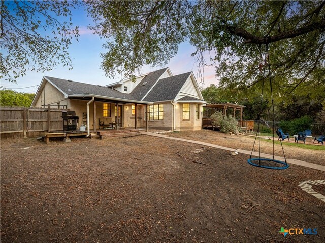 back of property at dusk featuring roof with shingles, fence, a pergola, and brick siding