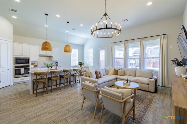 living room with an inviting chandelier, vaulted ceiling, a healthy amount of sunlight, and light hardwood / wood-style flooring