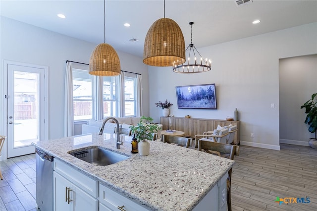 kitchen with a center island with sink, hanging light fixtures, sink, white cabinetry, and light hardwood / wood-style flooring