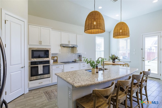 kitchen with stainless steel appliances, hanging light fixtures, sink, white cabinets, and a kitchen island with sink