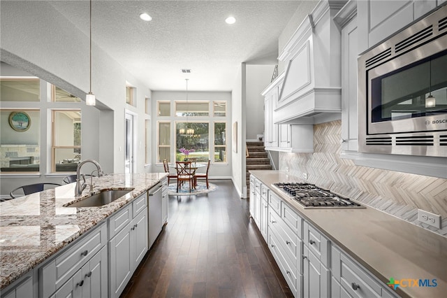 kitchen with dark wood-type flooring, custom range hood, decorative backsplash, appliances with stainless steel finishes, and a sink