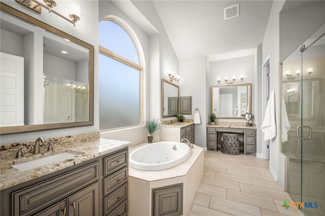 full bathroom featuring visible vents, two vanities, a stall shower, a tub with jets, and a sink