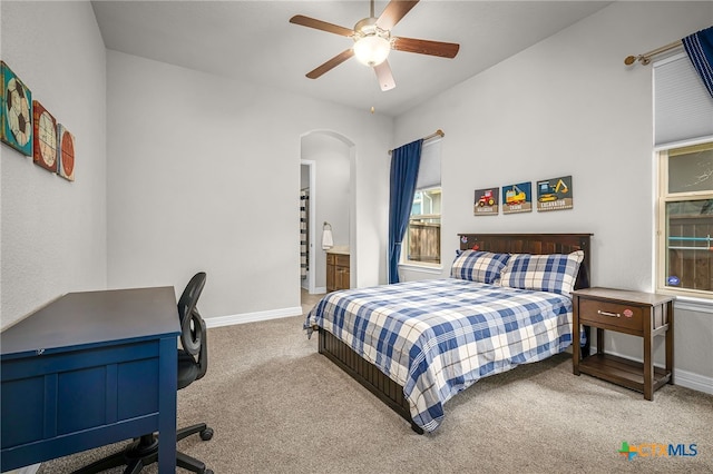 carpeted bedroom featuring baseboards, arched walkways, ensuite bathroom, and a ceiling fan