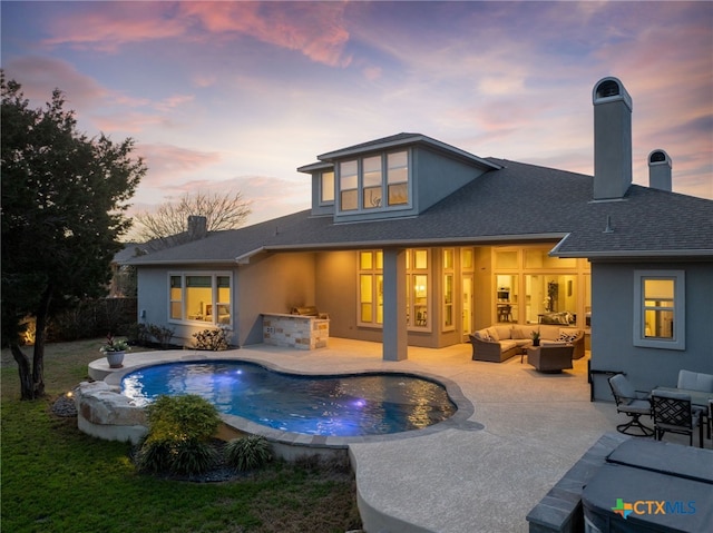 back of house at dusk featuring an outdoor kitchen, an outdoor hangout area, a chimney, and a patio