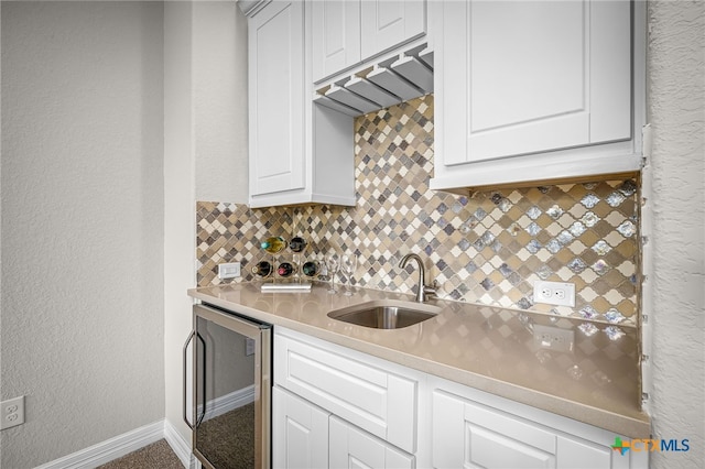 kitchen with tasteful backsplash, beverage cooler, light countertops, white cabinets, and a sink