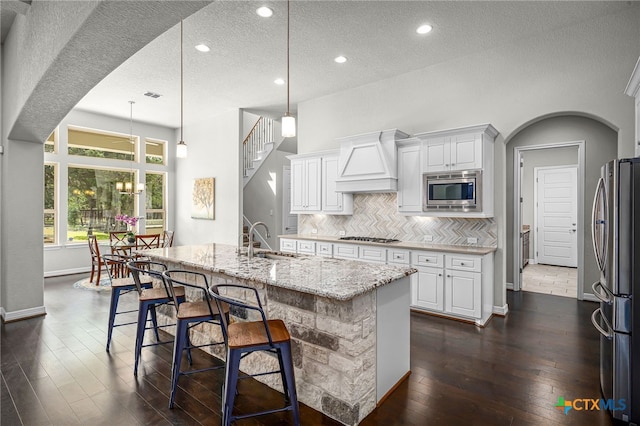 kitchen featuring a sink, light stone counters, backsplash, stainless steel appliances, and custom exhaust hood