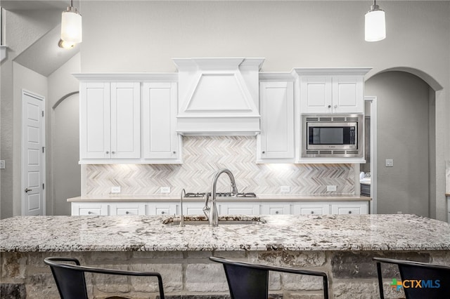 kitchen with stainless steel microwave, tasteful backsplash, light stone countertops, and arched walkways