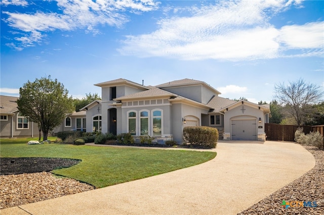 mediterranean / spanish house featuring a front yard, fence, stucco siding, concrete driveway, and a garage