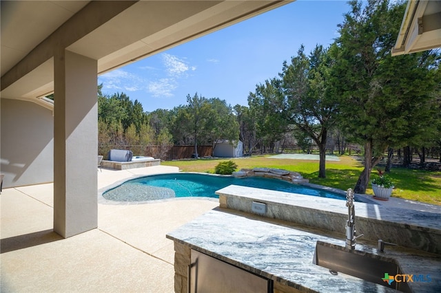 outdoor pool with fence, a patio area, a storage shed, an outbuilding, and a sink