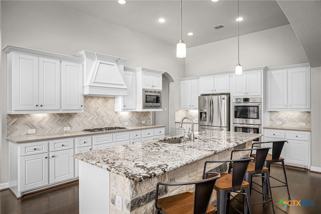 kitchen featuring custom exhaust hood, arched walkways, a sink, stainless steel appliances, and white cabinetry