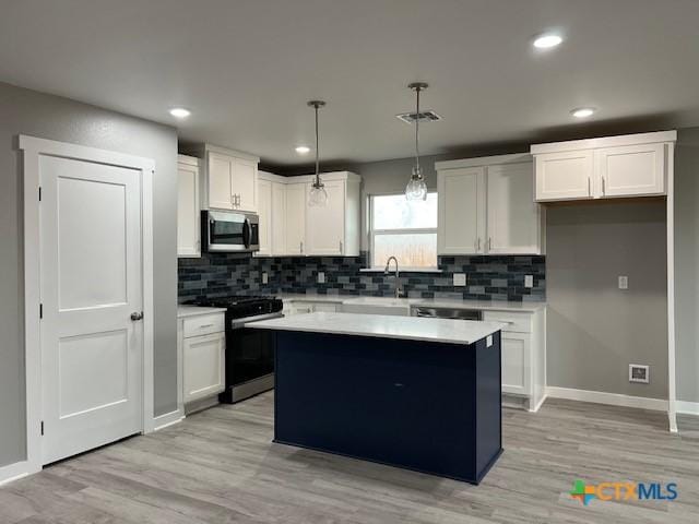 kitchen with white cabinets, gas range, stainless steel microwave, light countertops, and pendant lighting