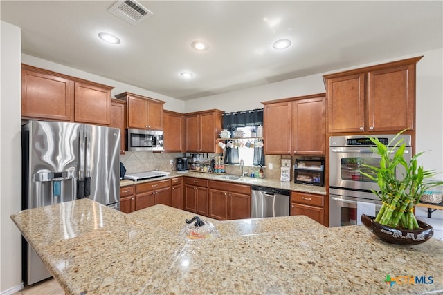 kitchen with decorative backsplash, light stone counters, sink, and appliances with stainless steel finishes