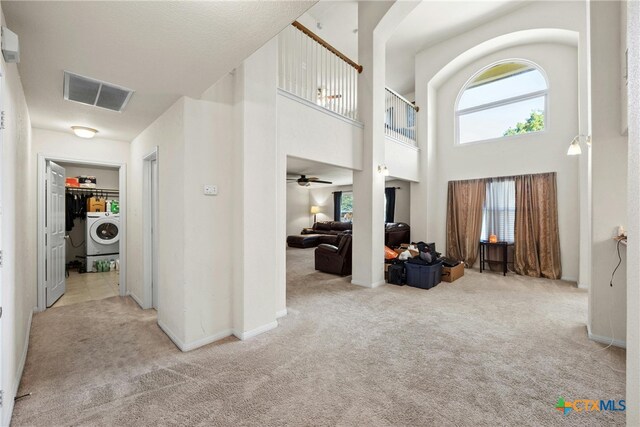 foyer entrance featuring ceiling fan, a high ceiling, light colored carpet, and washer / clothes dryer