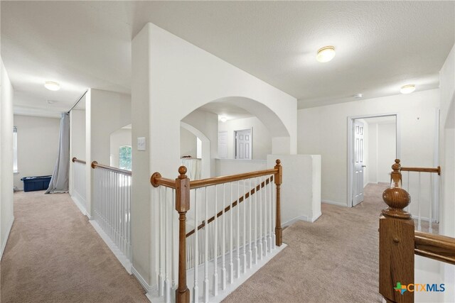 hallway with light colored carpet and a textured ceiling