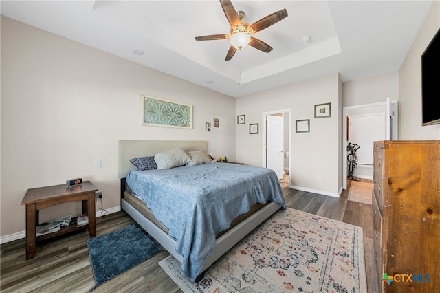 bedroom with dark wood-type flooring, ceiling fan, a raised ceiling, and connected bathroom