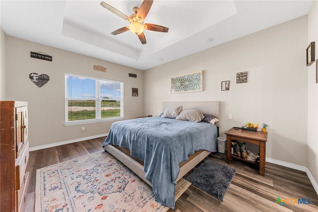 bedroom with hardwood / wood-style flooring, ceiling fan, and a raised ceiling