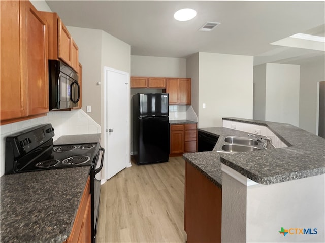 kitchen featuring decorative backsplash, light wood-type flooring, sink, black appliances, and an island with sink