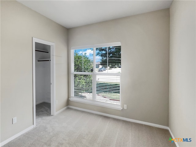 unfurnished bedroom featuring a spacious closet, a closet, and light colored carpet