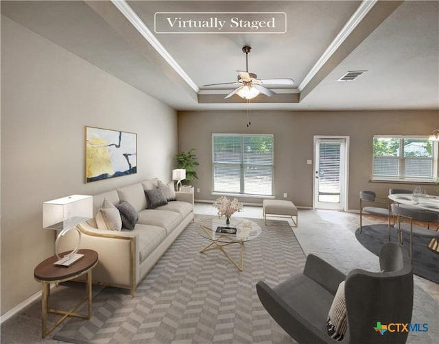 carpeted living room with ceiling fan, a healthy amount of sunlight, ornamental molding, and a tray ceiling