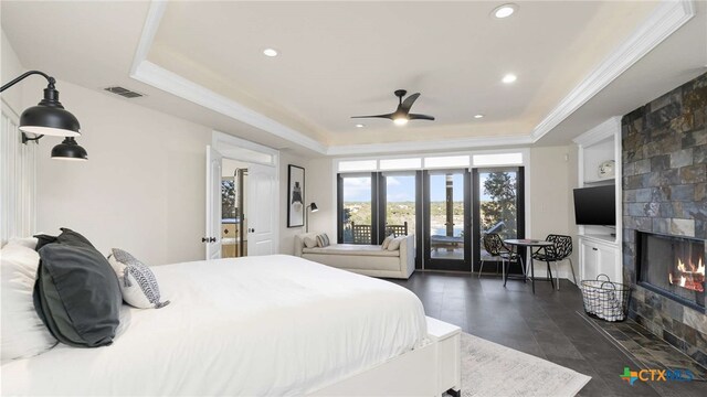 bedroom featuring ceiling fan, a tiled fireplace, and a tray ceiling