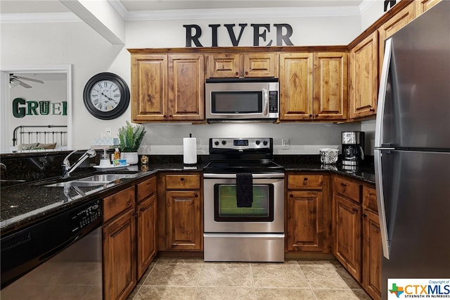 kitchen with a sink, appliances with stainless steel finishes, brown cabinetry, dark stone countertops, and crown molding