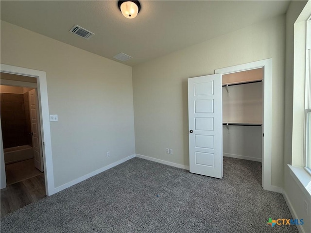 unfurnished bedroom with a spacious closet, a closet, and dark colored carpet