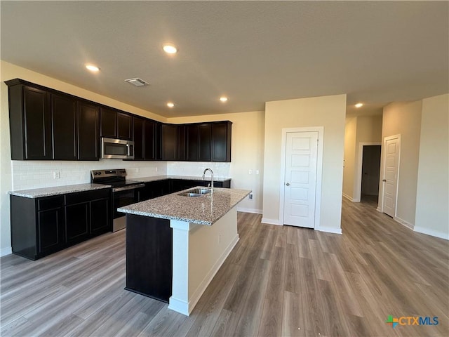 kitchen featuring sink, light stone counters, tasteful backsplash, a center island with sink, and stainless steel appliances