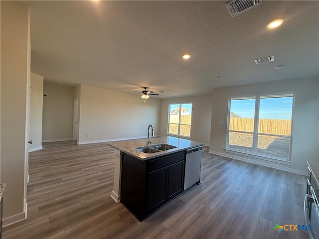 kitchen featuring sink, dark hardwood / wood-style flooring, stainless steel dishwasher, light stone countertops, and a center island with sink