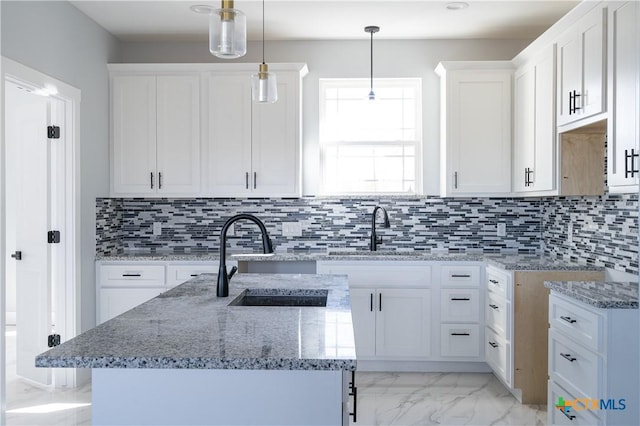 kitchen featuring white cabinets, sink, decorative backsplash, an island with sink, and decorative light fixtures