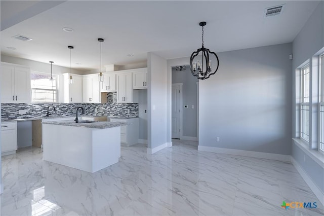 kitchen featuring white cabinetry, a notable chandelier, backsplash, decorative light fixtures, and a kitchen island with sink