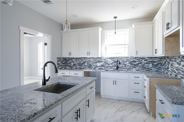 kitchen with decorative backsplash, white cabinetry, sink, and hanging light fixtures