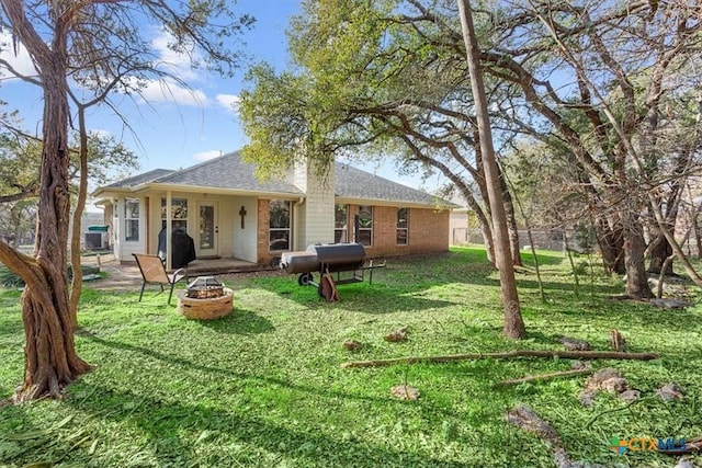 back of house with a lawn and a fire pit