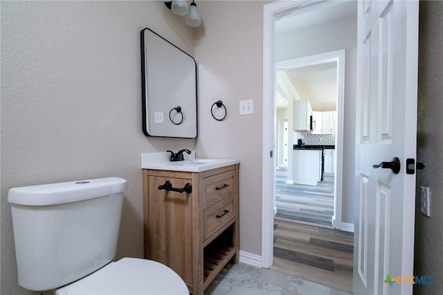 half bathroom featuring baseboards, tasteful backsplash, toilet, and vanity